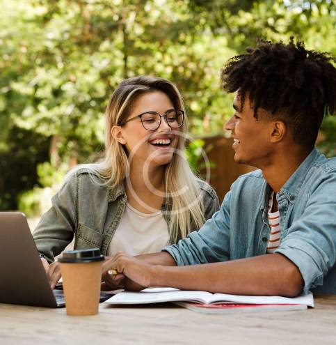 Positive young multiethnic couple spending time together at the park, studying while sitting at the table with laptop